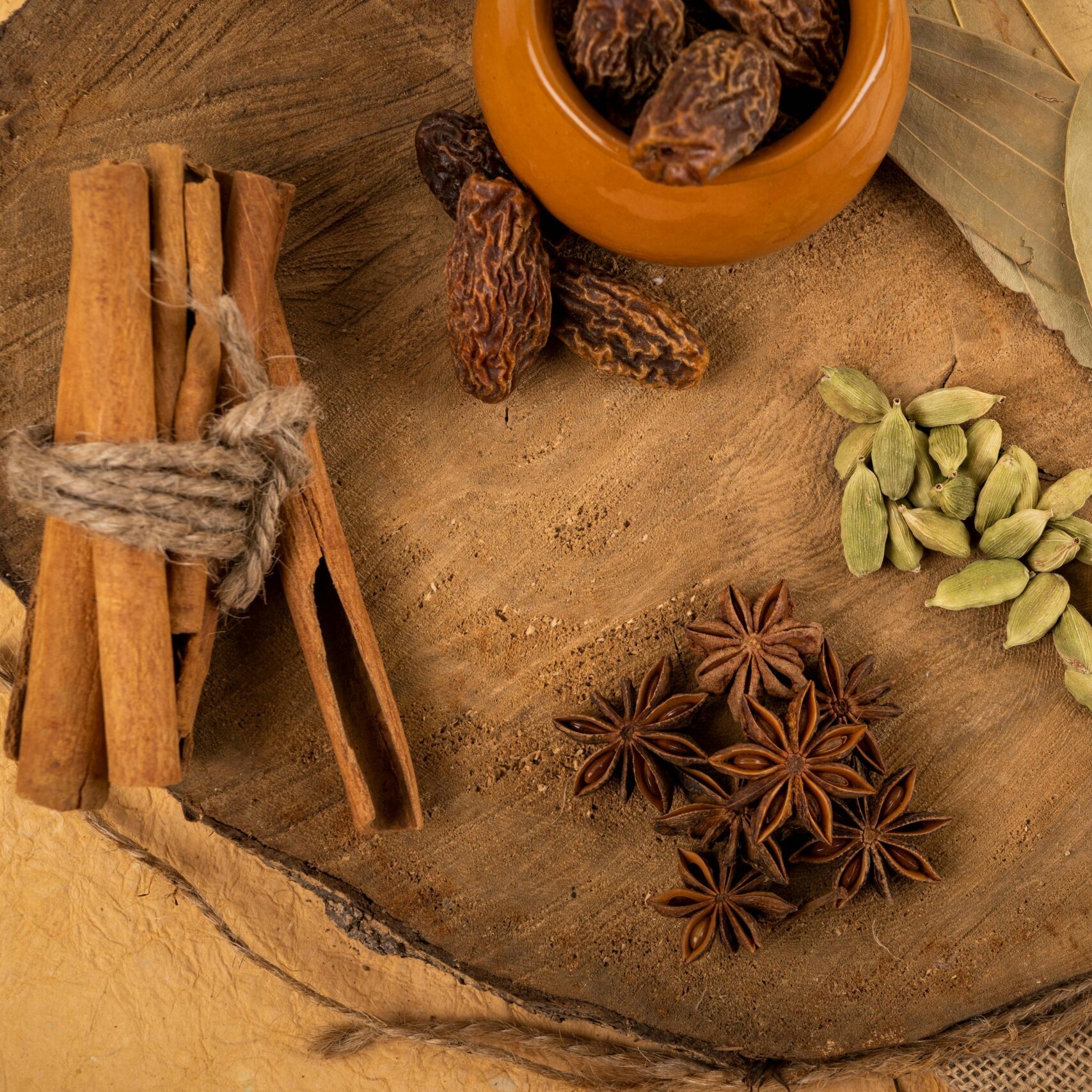 A collection of Indian spices including cardamom, star anise, and bay leaves on a wooden board.